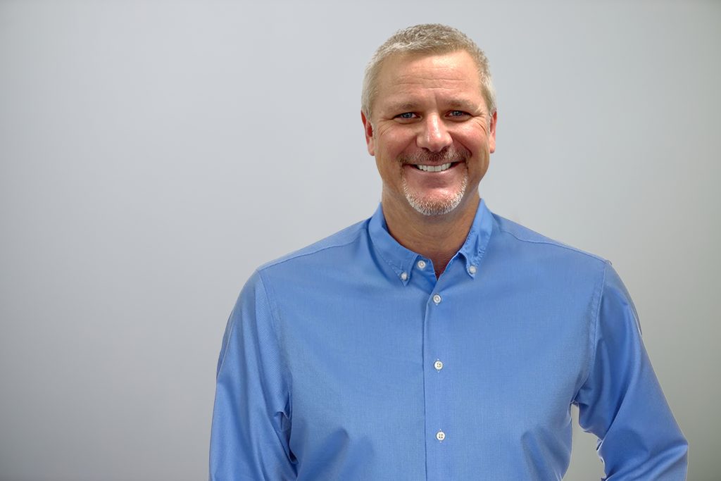 Bert Woerner wearing a blue button up shirt in front of a grey background.
